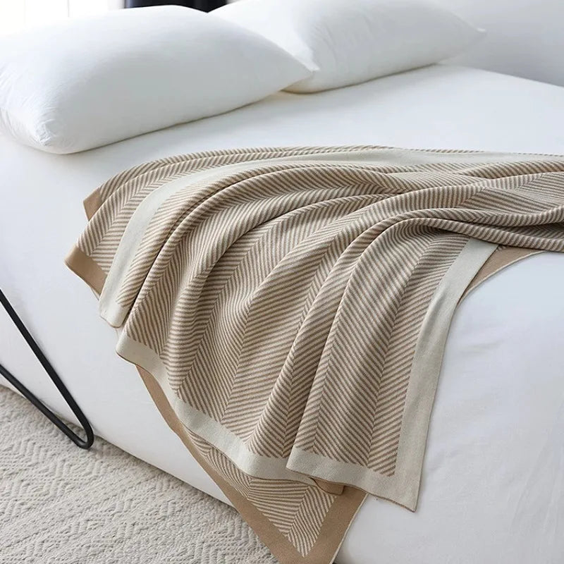 Couverture en tricot rayée beige et blanche sur un lit avec des coussins blancs.