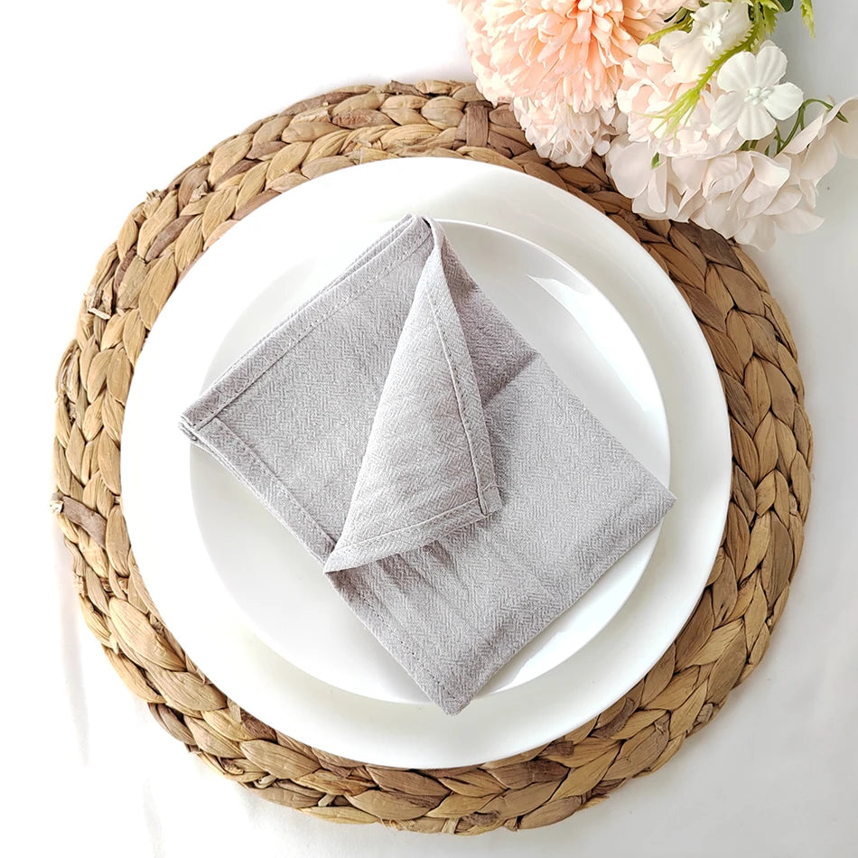 Un gros plan d'une assiette blanche posée sur un set de table en fibres tressées, accompagnée d'une serviette grise pliée.