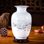 Vase en céramique blanc décoré d'un paysage hivernal enneigé, avec des montagnes et des maisons en arrière-plan.