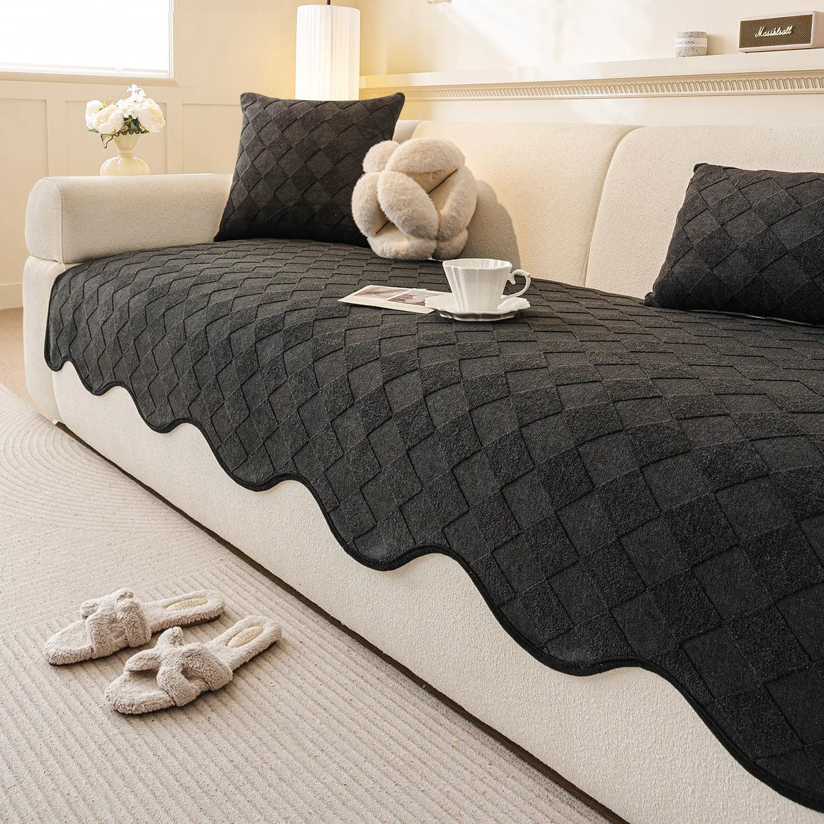 Ce salon douillet présente une décoration élégante avec un canapé beige, des coussins en laine noirs et un plaid motif losange posé dessus, créant une ambiance chaleureuse et apaisante.