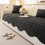 Ce salon douillet présente une décoration élégante avec un canapé beige, des coussins en laine noirs et un plaid motif losange posé dessus, créant une ambiance chaleureuse et apaisante.