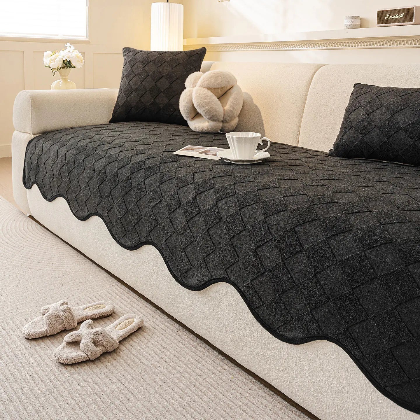 Ce salon douillet présente une décoration élégante avec un canapé beige, des coussins en laine noirs et un plaid motif losange posé dessus, créant une ambiance chaleureuse et apaisante.