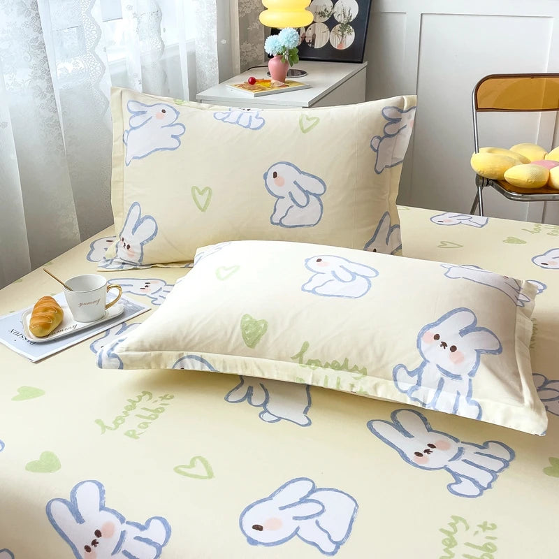 Ensemble de literie avec motif de lapins mignons en bleu, vert et jaune sur fond beige clair, créant une ambiance douce et rafraîchissante dans la chambre.