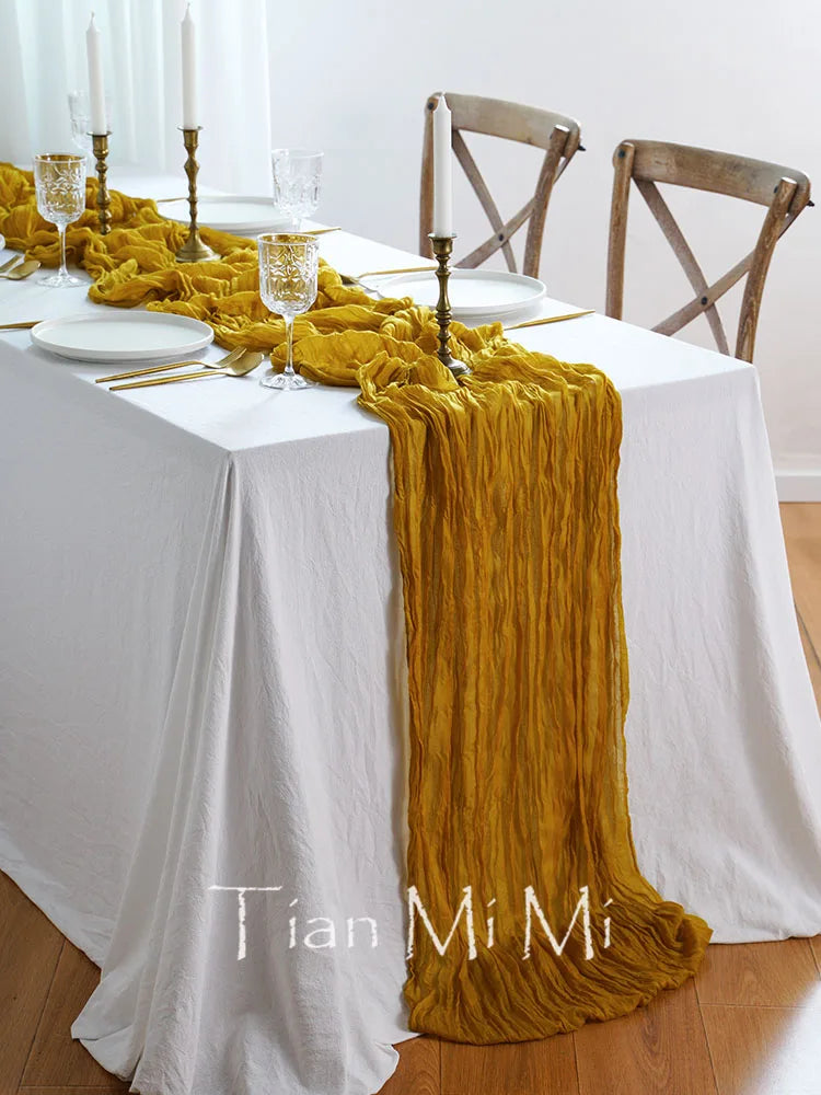 Table décorée avec nappe blanche, chemin de table en velours jaune moutarde, candélabres et verres sur la table.