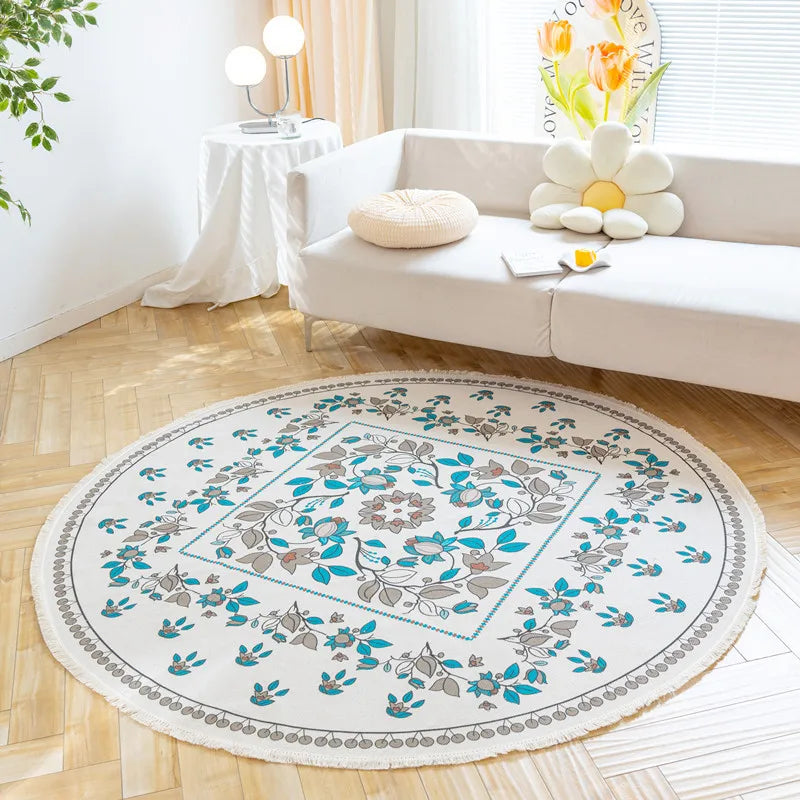 Un tapis rond décoré de motifs floraux bleus et gris, dans un salon lumineux avec un canapé blanc et des plantes.