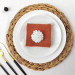 Un magnifique arrangement avec une serviette rouge et une fleur blanche sur une assiette blanche posée sur un support en fibres tressées.