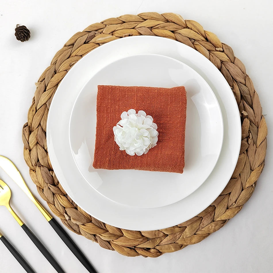 Un magnifique arrangement avec une serviette rouge et une fleur blanche sur une assiette blanche posée sur un support en fibres tressées.