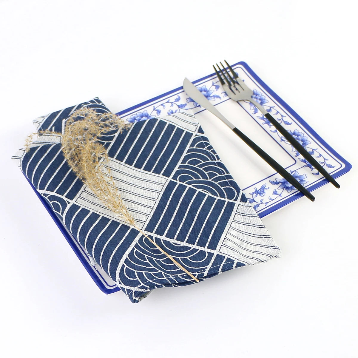 Cette image présente un ensemble de table et de couverts avec un motif bleu et blanc élégant, ainsi qu'une décoration végétale en fibre naturelle.