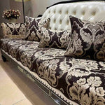 Sofa rembourré blanc avec des coussins décoratifs aux motifs floraux et damassés bruns et beige, entouré de plantes dans un intérieur élégant.