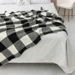 Une couverture à motifs géométriques noirs et blancs est étendue sur un lit, créant une atmosphère sophistiquée et épurée dans la chambre.