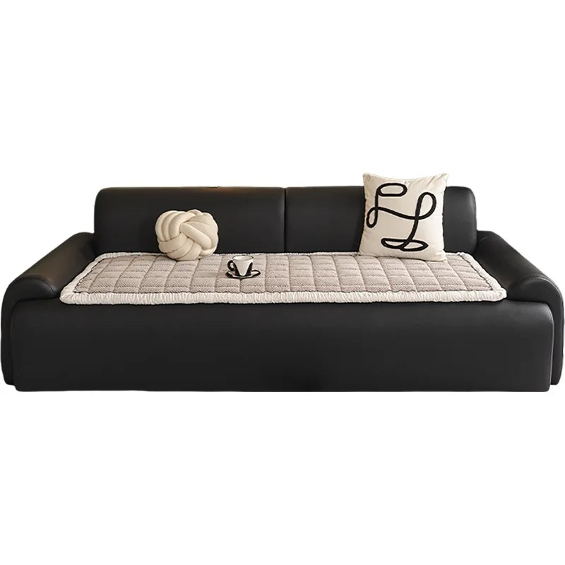 Canapé moderne en cuir noir avec des coussins décoratifs et un quilting en tissu crème.