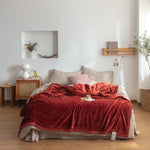 Chambre cosy avec un lit double, des coussins roses, un couvre-lit rouge en velours et une décoration minimaliste et chaleureuse.