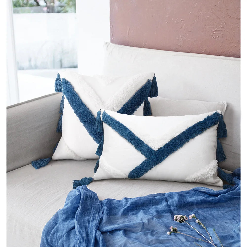 Coussin blanc et bleu avec franges, posé sur un canapé gris, accompagné d'une couverture en lin bleu.