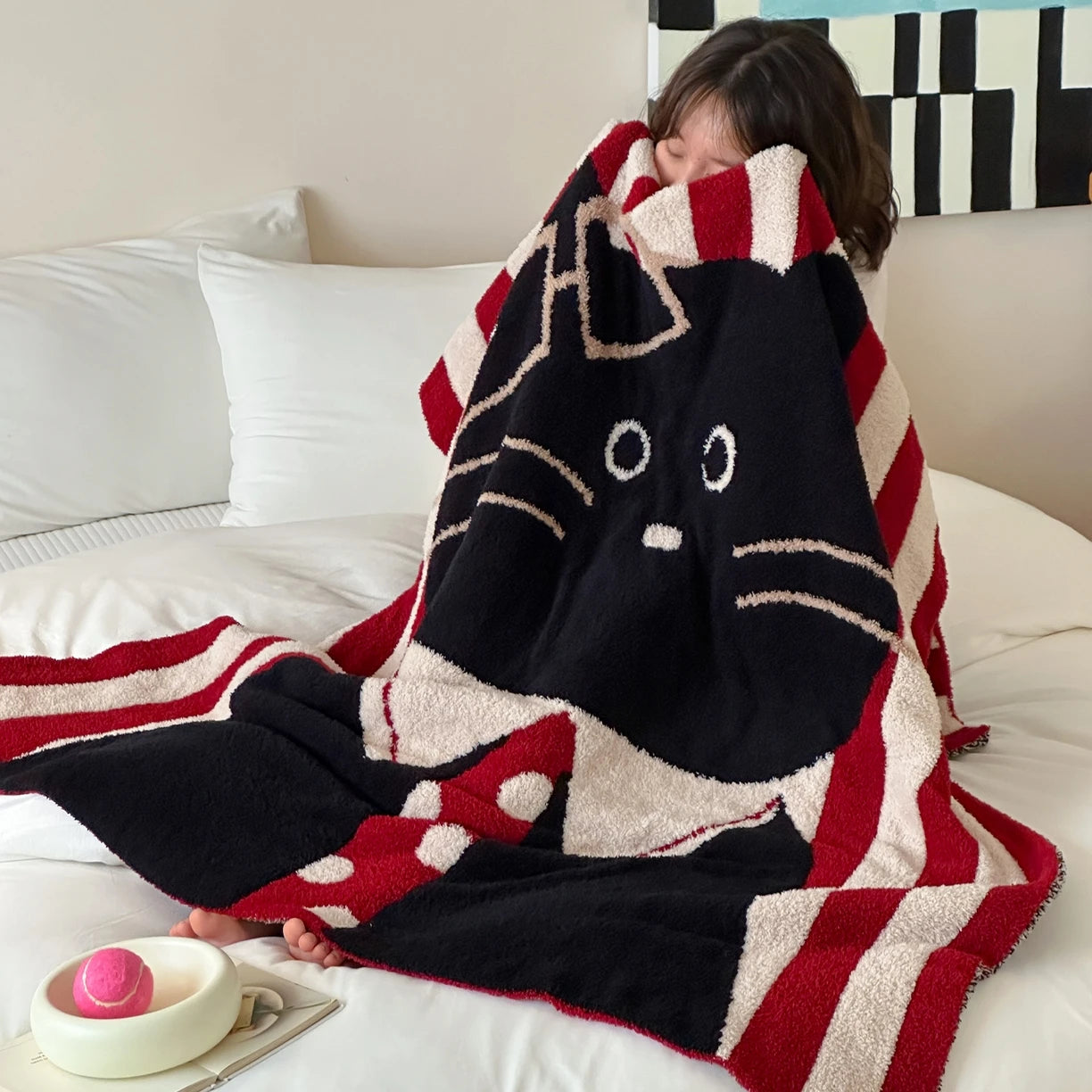Une couverture moelleuse et rayée de rouge et de noir, avec un motif de chat mignon, offre un confort douillet sur le lit.