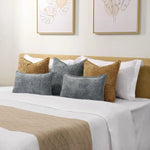 Coussins décoratifs en velours gris et beige sur un lit avec des draps blancs et un couvre-lit en satin, créant une ambiance apaisante et élégante dans cette chambre.