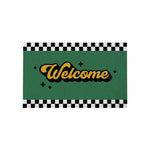 Tapis d'entrée vert avec lettrage doré et bordure à damier noir et blanc pour accueillir les visiteurs.