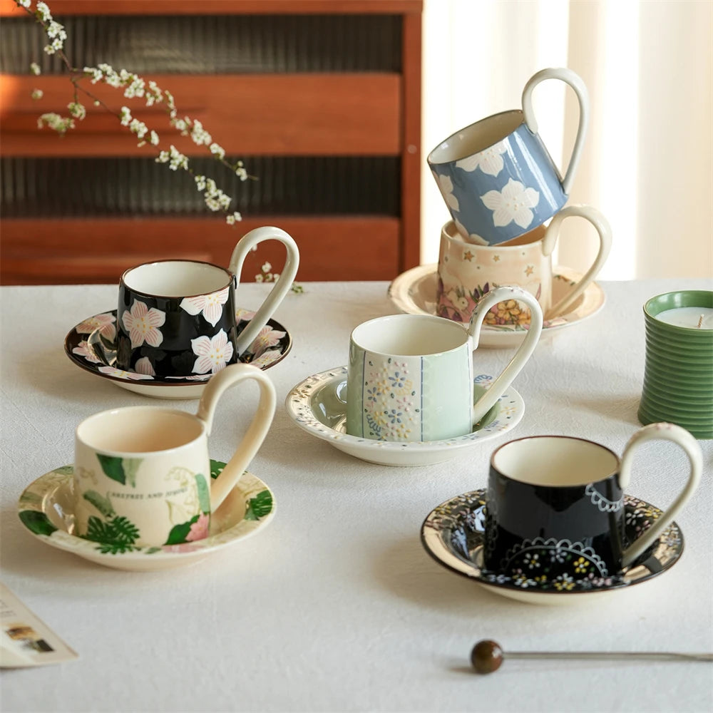 Une collection de tasses et soucoupes en céramique décorées de motifs floraux colorés, disposées sur une surface blanche avec une plante en arrière-plan.