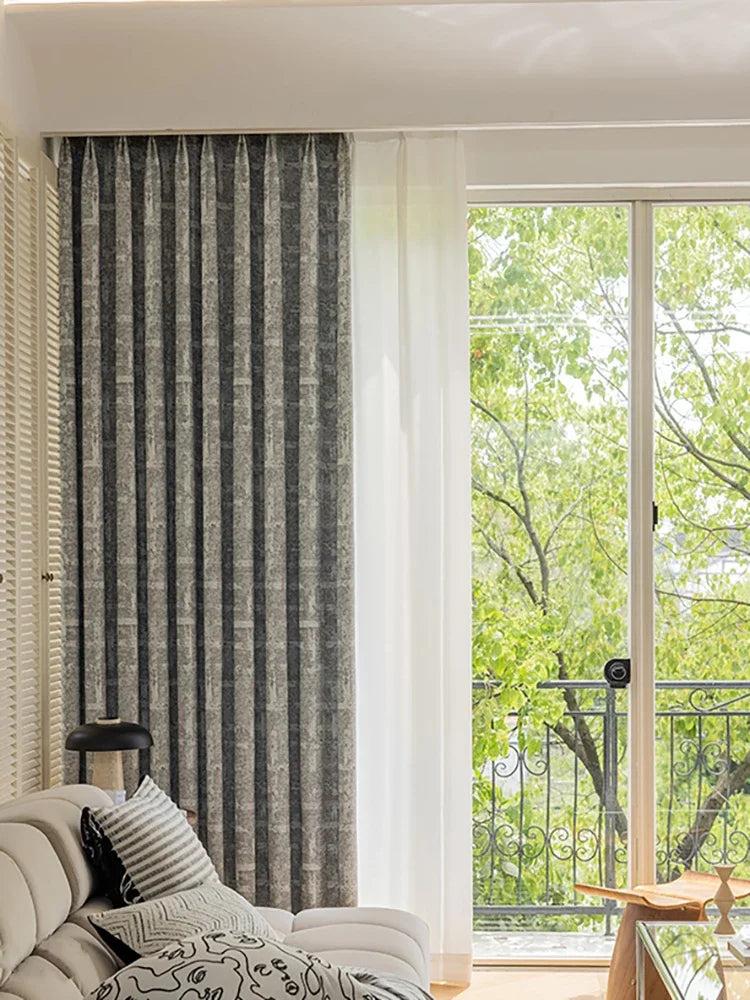 Rideau occultant gris foncé pour salon moderne, offrant élégance et intimité; vue sur balcon verdoyant avec lumière naturelle.