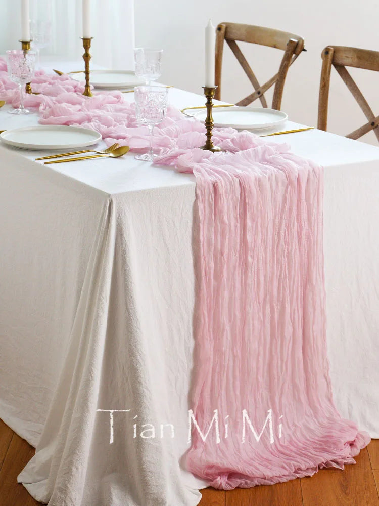 Cette image montre une table de salle à manger élégamment décorée avec une nappe blanche, des chandeliers dorés, des verres de cristal et un chemin de table en rose pâle, créant une ambiance chaleureuse et raffinée.