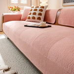 Un élégant canapé rose pâle avec des coussins décoratifs, placé dans un intérieur lumineux avec des fenêtres, un tapis gris et une belle fleur blanche sur une tablette noire.