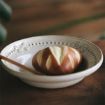 Sur une assiette blanche décorée, se trouve une pomme fraîche, avec une belle peau brillante et une couleur rouge vif.