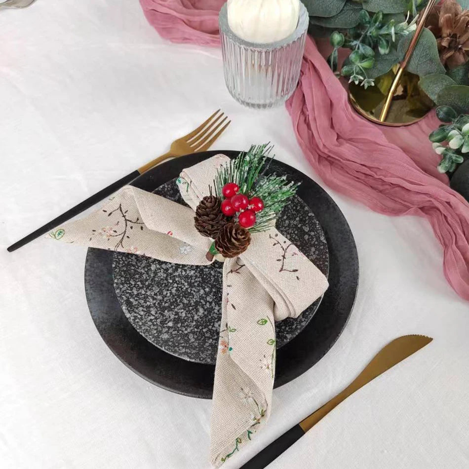 Une table élégante avec une décoration hivernale, avec une serviette de table ornée de motifs floraux, des cônes de pin et des baies rouges, un beau contraste avec un fond noir et rose.