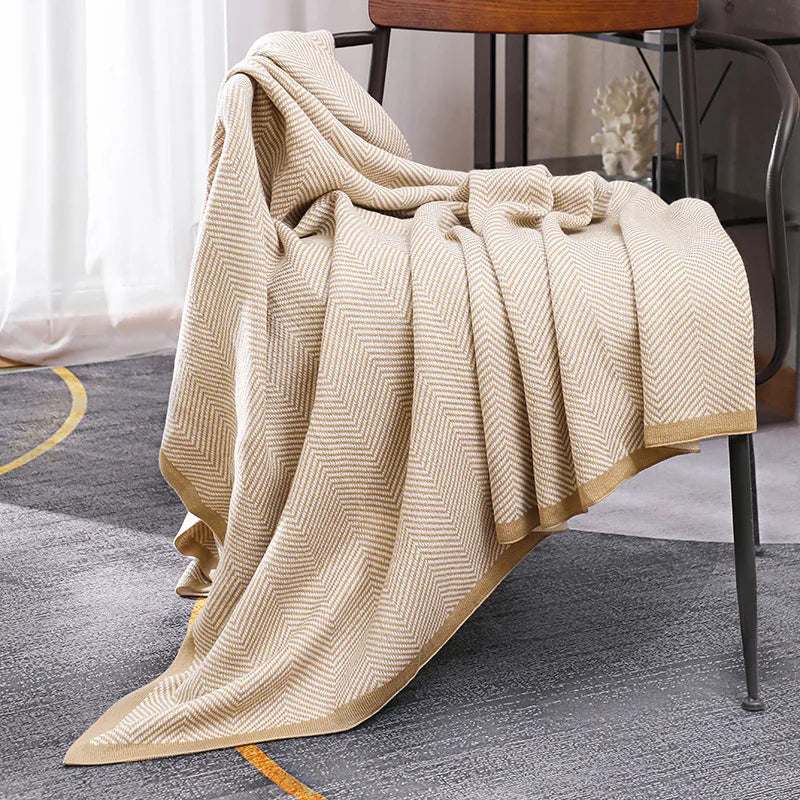 Une couverture beige texturée avec des motifs géométriques, posée sur une chaise en bois dans une pièce éclairée.