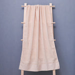 Une serviette de bain beige suspendue sur un portant en bois sur un fond gris foncé.