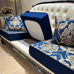 Un canapé blanc capitonné avec des coussins en tissu bleu foncé et beige aux motifs floraux élégants, créant une ambiance de luxe et de raffinement.