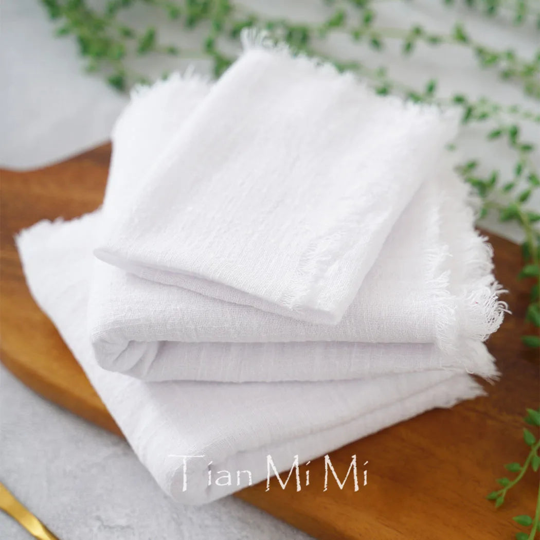 Une pile de serviettes blanches duveteuses posées sur une surface en bois avec des plantes vertes en arrière-plan.