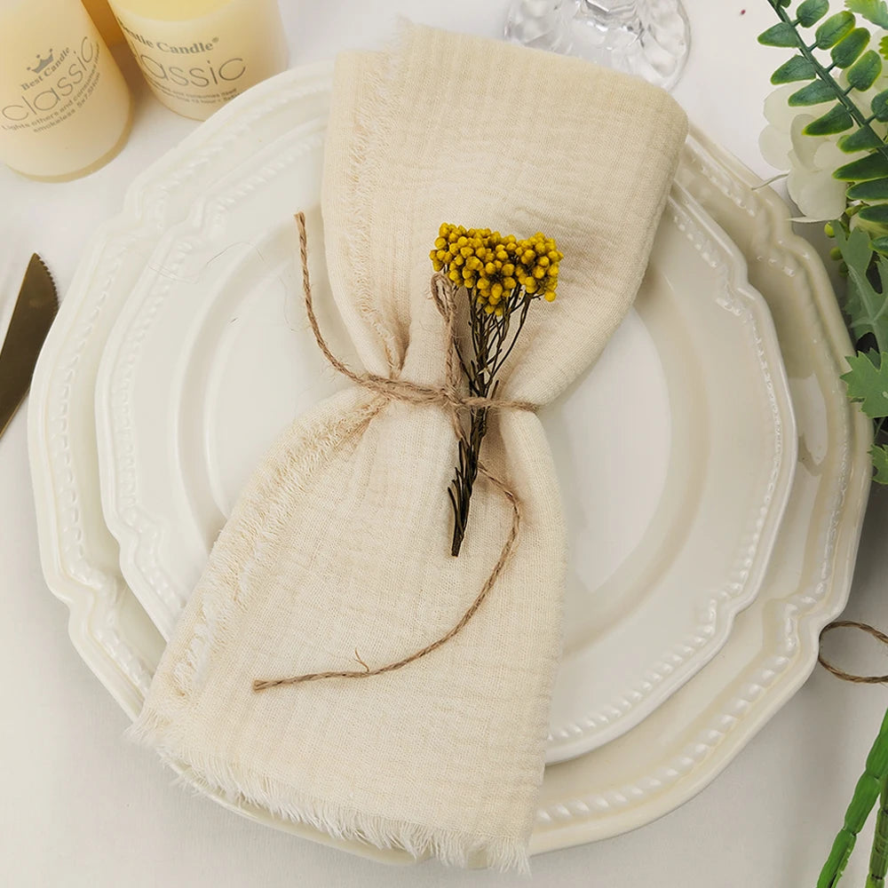 Un serviette beige enroulée avec un bouquet de fleurs jaunes sur une assiette blanche, complétée par des accessoires et des plantes vertes.