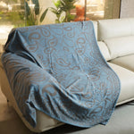 Couverture décorative pliée avec un motif abstrait bleu sur fond blanc, créant une atmosphère apaisante dans une pièce ensoleillée.