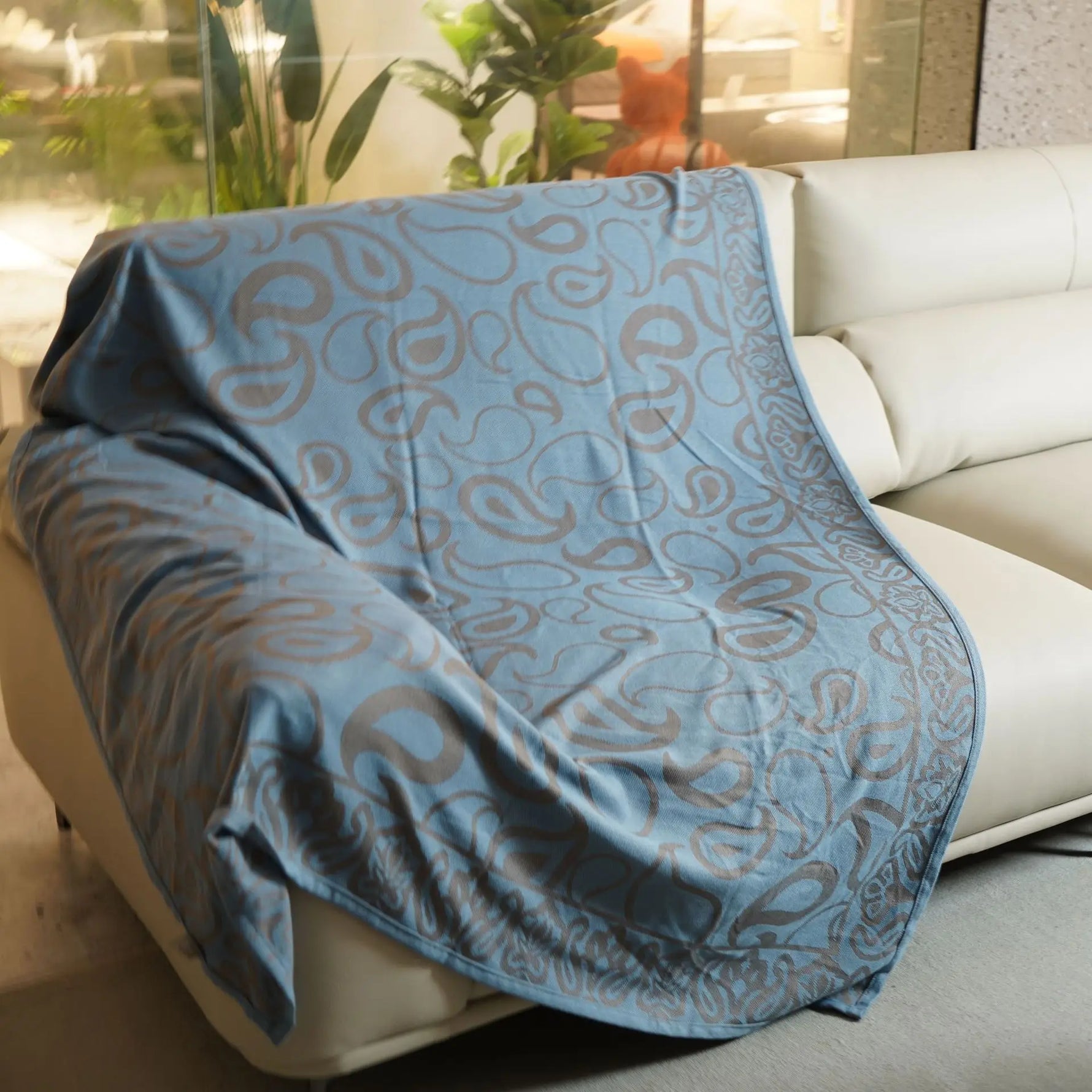 Couverture décorative pliée avec un motif abstrait bleu sur fond blanc, créant une atmosphère apaisante dans une pièce ensoleillée.