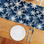 Arrangement de table festive avec motif de flocons de neige bleus sur un fond sombre, assiette blanche et couverts sur une surface en bois.