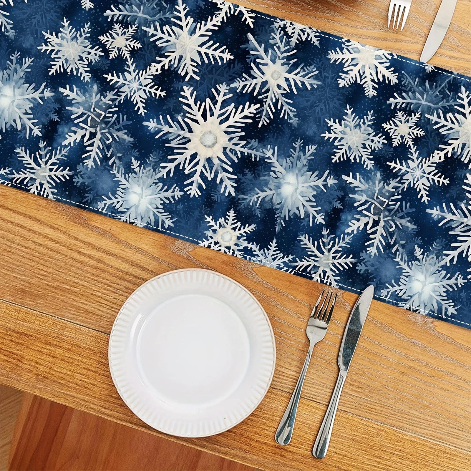 Arrangement de table festive avec motif de flocons de neige bleus sur un fond sombre, assiette blanche et couverts sur une surface en bois.