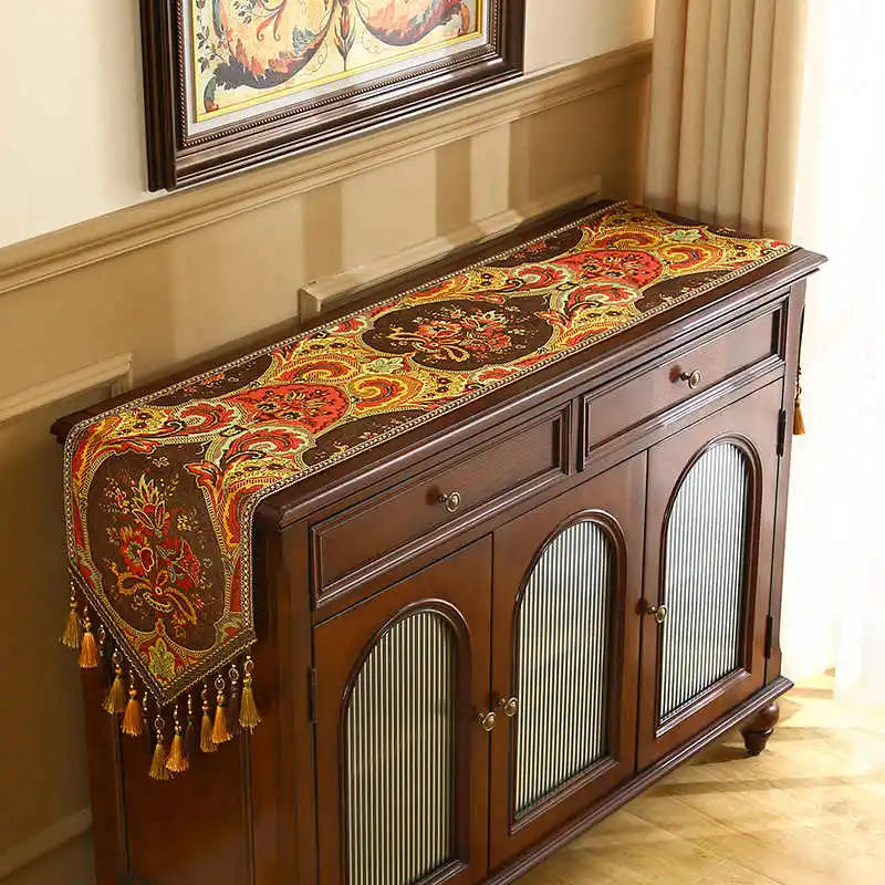 Ce meuble de style ancien est orné d'un magnifique chemin de table coloré, aux motifs floraux et décoratifs, qui ajoute une touche d'élégance à la pièce.