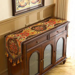 Ce meuble de style ancien est orné d'un magnifique chemin de table coloré, aux motifs floraux et décoratifs, qui ajoute une touche d'élégance à la pièce.