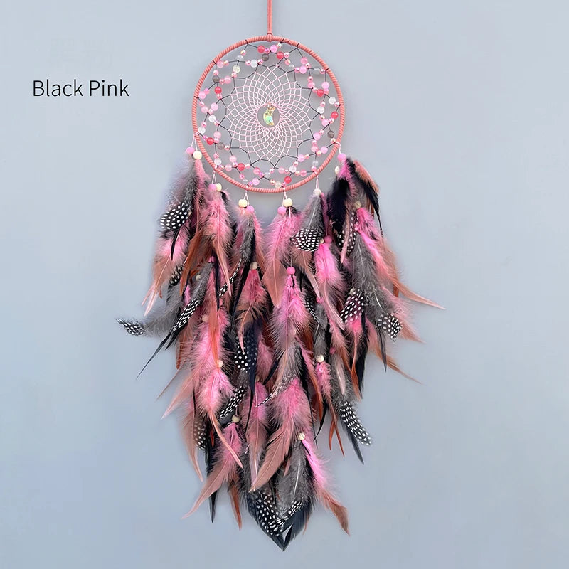 Un capteur de rêves décoratif en forme de cercle, avec des plumes roses et noires ornées de perles, suspendu par un fil de couleur rose.