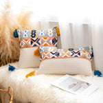 Deux coussins décoratifs aux motifs ethniques colorés, sur une fourrure blanche, avec des plumes et des livres posés à côté.