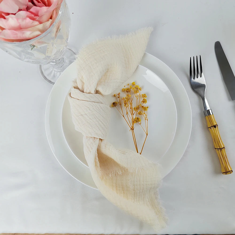 Une table élégante avec une assiette blanche, une serviette en tissu beige, une fourchette et un couteau dorés, ainsi qu'une fleur jaune posée sur l'assiette.