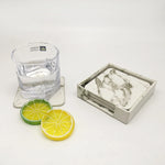Un verre en cristal rempli d'eau et entouré de morceaux de citron vert et jaune, posé sur un support en marbre blanc avec une boîte de rangement en marbre.