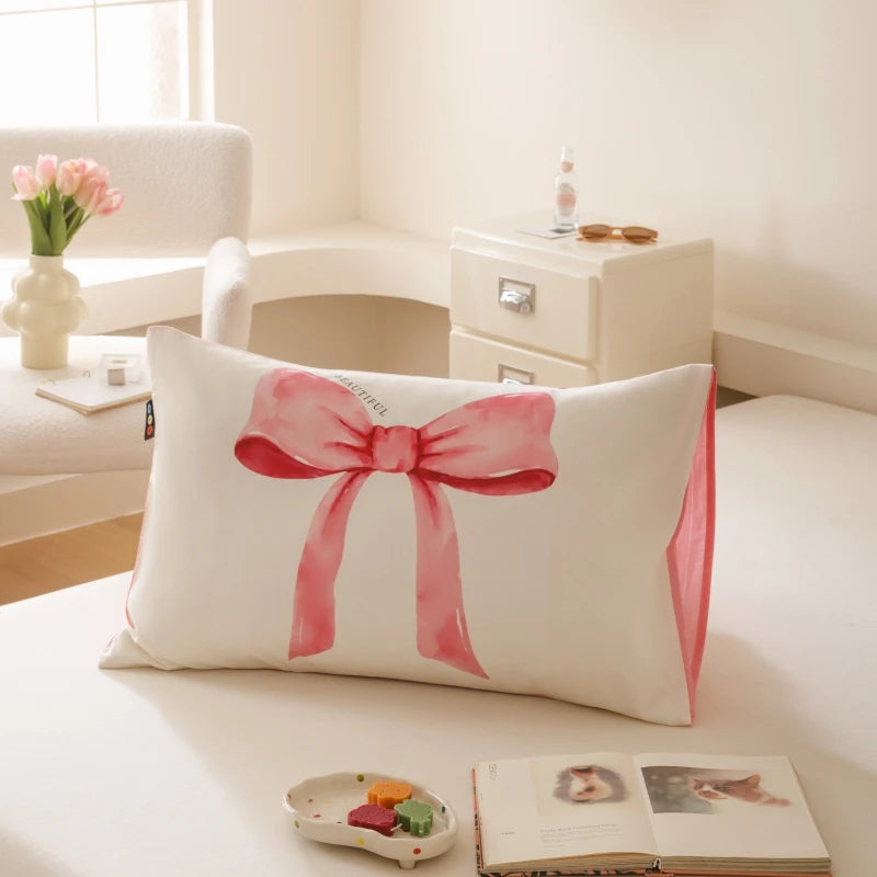 Coussin décoratif blanc avec un noeud rouge, posé sur une table de chevet dans un intérieur lumineux et cosy.