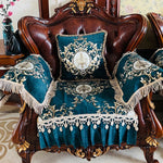 Le canapé en cuir brun foncé est orné de coussins décoratifs en velours bleu et or, avec des motifs floraux élégants et une frange luxueuse, créant une atmosphère raffinée et sophistiquée dans cette pièce d'intérieur.