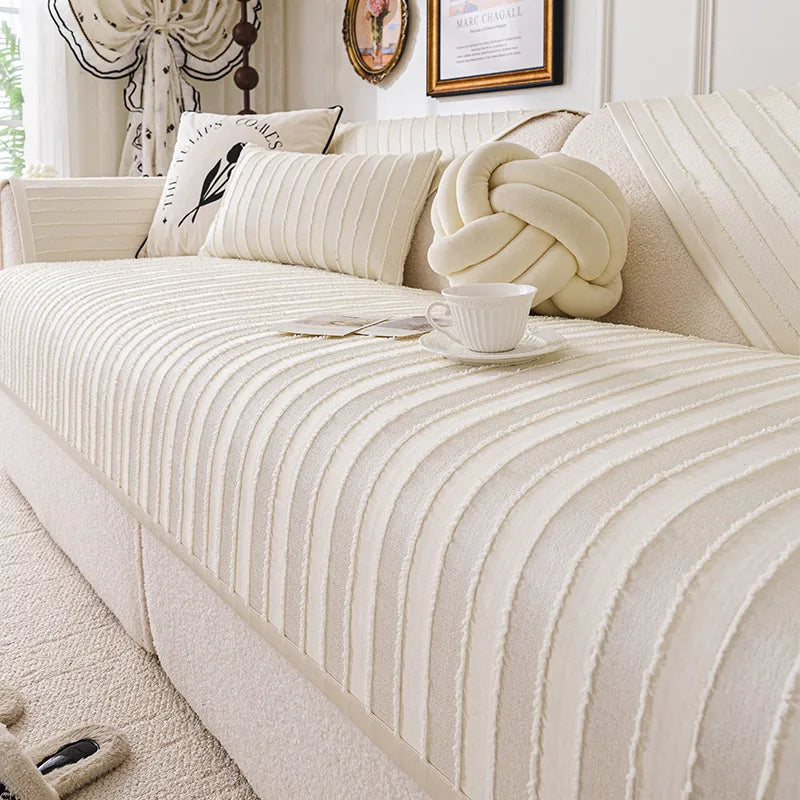 Un canapé moelleux et capitonné dans un salon élégant, avec des coussins et un vase blanc posés sur le tissu crème aux rayures subtiles, créant une ambiance chaleureuse et reposante.