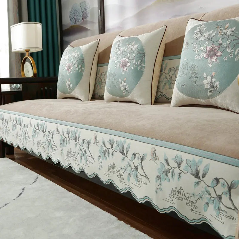 Un canapé moelleux et confortable, avec des coussins ornés de motifs floraux et paysagers dans des tons bleus et beiges, créant une atmosphère relaxante et élégante.