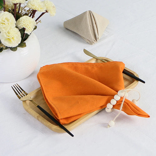 Une table de restaurant élégante avec de belles fleurs et des couverts en or sur une serviette orange.