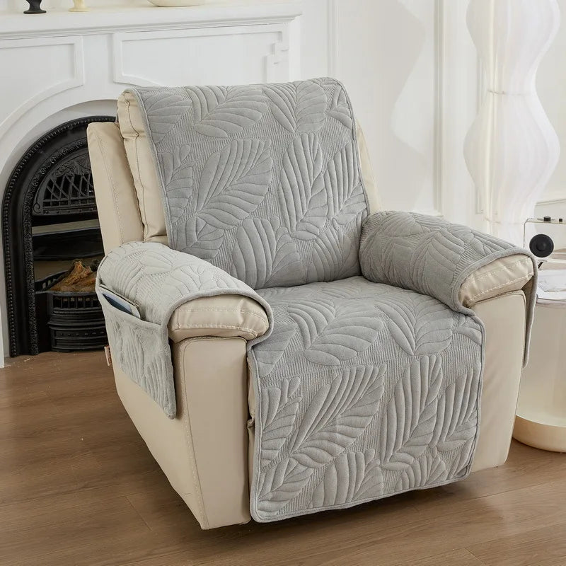 Un fauteuil confortable avec un motif de feuilles gris clair, placé dans une pièce blanche et bien éclairée, avec une cheminée ancienne en arrière-plan.