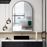 Cette image montre une élégante salle de bain au design moderne, avec un miroir arrondi encadré de noir, des luminaires dorés, une baignoire blanche et un meuble de rangement noir avec un plateau en marbre blanc.