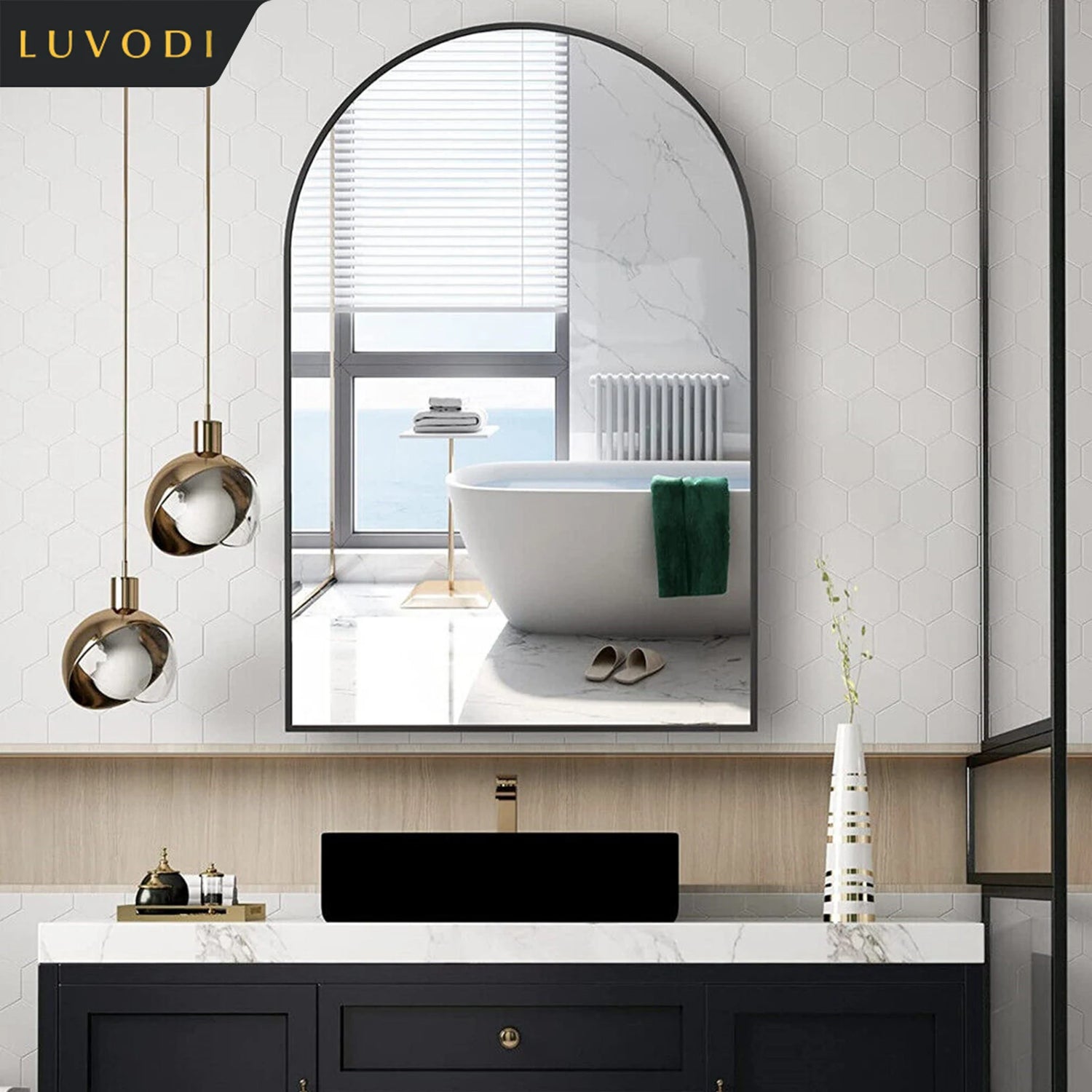 Cette image montre une élégante salle de bain au design moderne, avec un miroir arrondi encadré de noir, des luminaires dorés, une baignoire blanche et un meuble de rangement noir avec un plateau en marbre blanc.