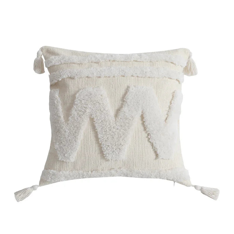 Une taie d'oreiller blanche décorative avec des motifs géométriques et des pompons aux coins.